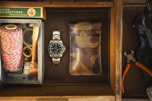 A drawer containing a roll of red and white string, several small tools, a wooden-handled pipe, a silver wristwatch, and a camouflage leather pouch—perhaps one of the SAMPLE SALE Green camo, stiff veg tan leather STRAP from the Secret Sale Department. Additionally, there is a box of matches labeled "Union Allumettière Bruxelles-Brussel" on the left.