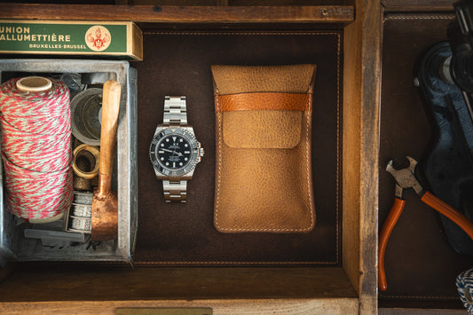 A neatly organized drawer contains a SAMPLE SALE Rugged chestnut watch with a cognac strap in a leather case protector, a coiled spool of red and white thread, metal wire, a small brass hammer, matches, and a pair of pliers—showcasing a mix of crafting tools and accessories.